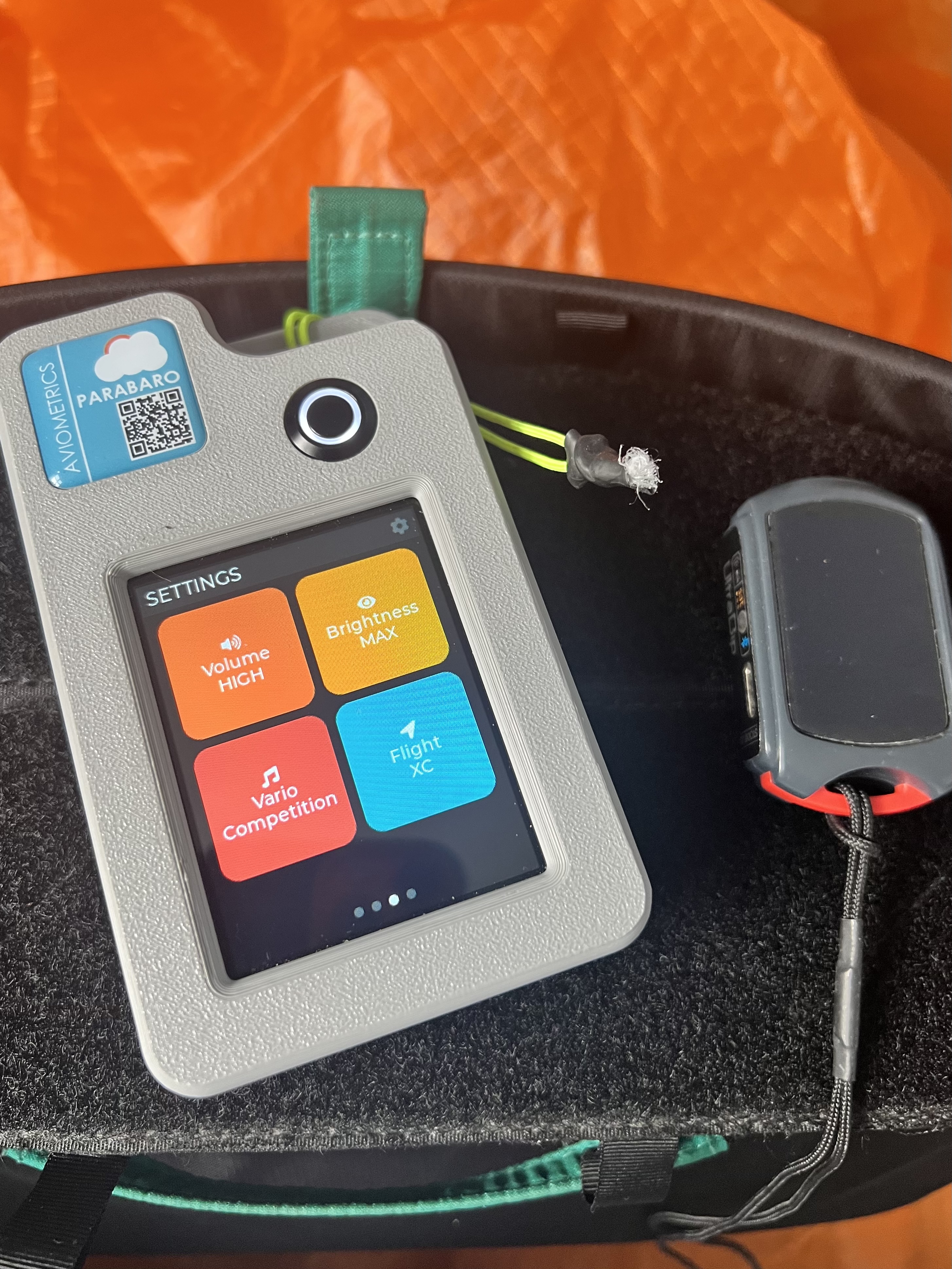 ParaBaro receiver in harness cockpit during flight with orange paraglider wing visible