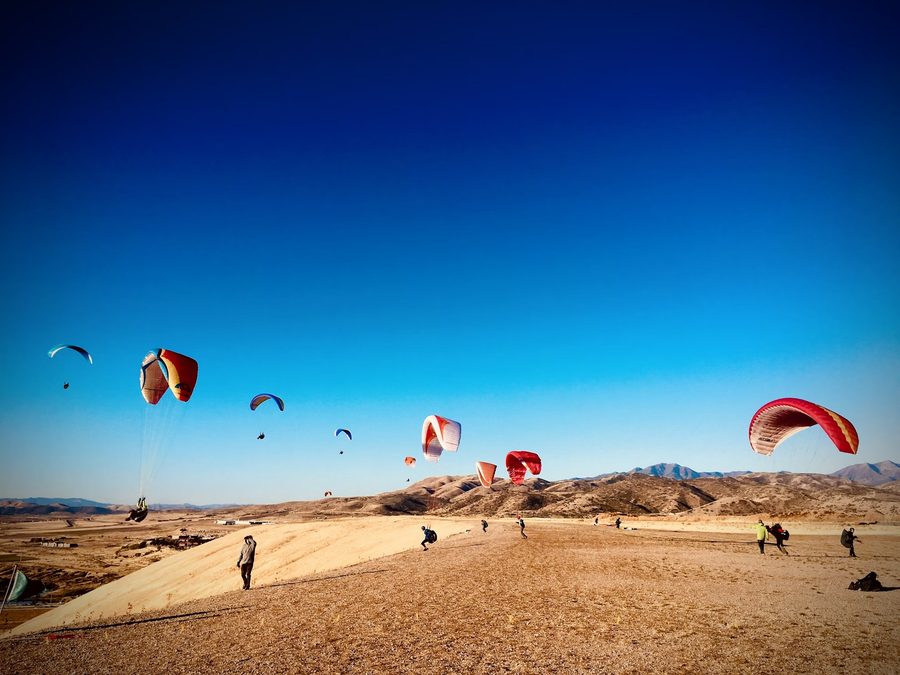 Multiple paragliders launching and thermalling over a desert landscape — competition conditions where weak thermal skill determines who stays up