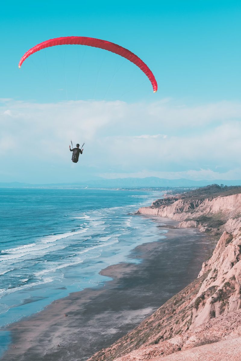 Paraglider soaring low along coastal cliffs in late light, working marginal lift close to the terrain