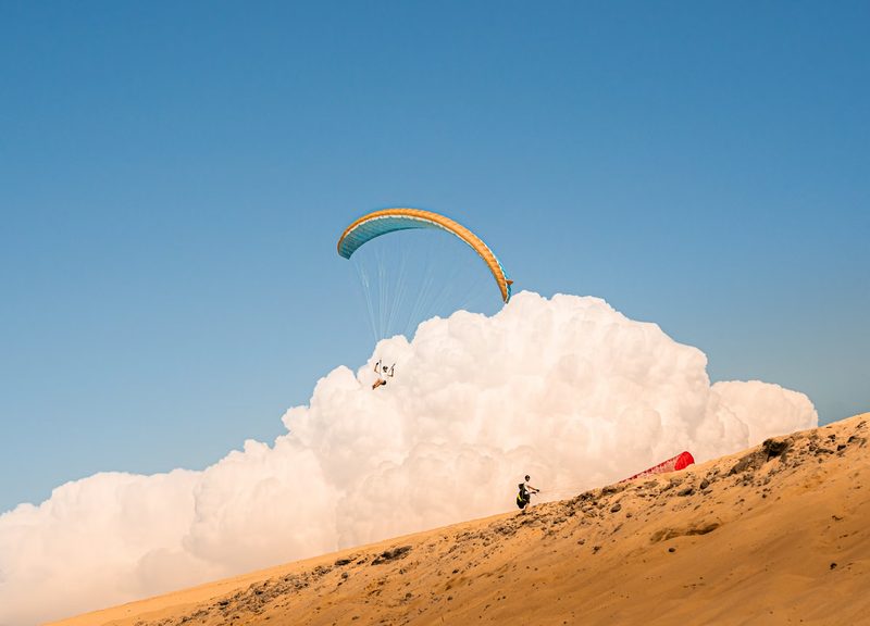 Paraglider soaring in front of a massive cumulus cloud formation — the kind of thermal structure ParaBaro's spatial detection was built to read