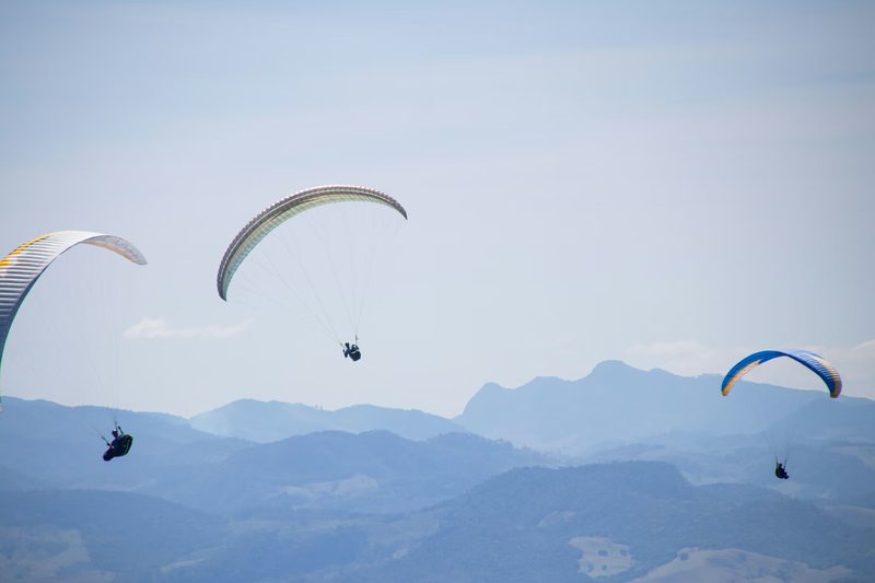 Three paragliders flying over misty mountain ridges, each relying on instruments that measure the wrong thing for collapse prediction