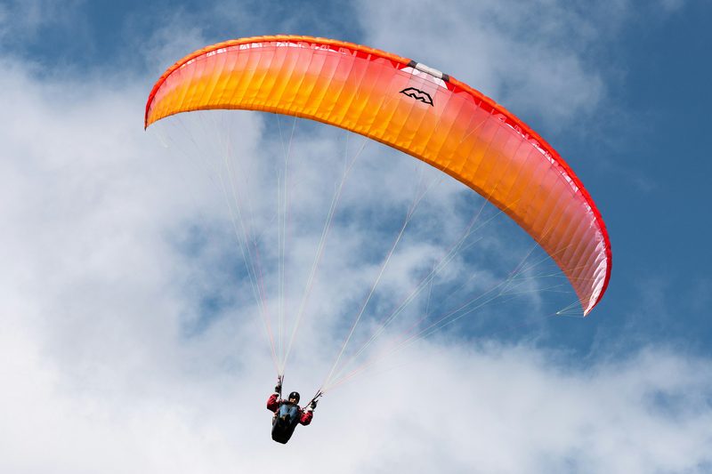 Close-up of paraglider orange wing in flight against blue sky, showing the canopy shape that generates differential pressure