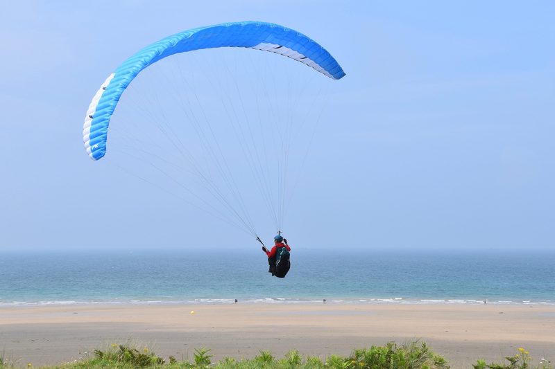 Paraglider with blue wing in flight showing full canopy structure — the shape maintained entirely by internal air pressure